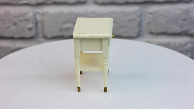 Toy wooden piece of furniture in studio. Tiny white nightstand with a cute drawer and shiny golden knob. Toy furniture circling isolated against wall background.