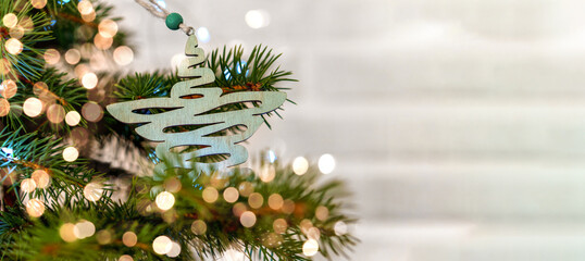 Christmas tree decorated with a star made from natural materials and a bokeh of lights on a white brick wall background. Eco-friendly lifestyle concept.