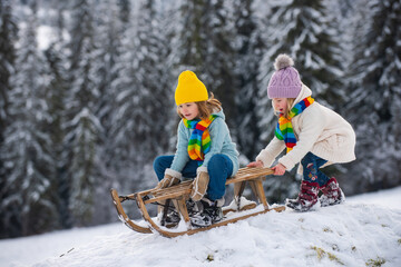 Cute girl and boy enjoying a sleigh ride. Children sledding in snow on winter park. Nature snowy...