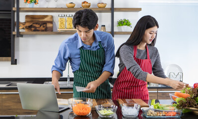 Young Asian chef couple helping each other to cook healthy food of salad from tasty organic...