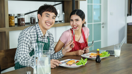 Romantic young Asian lovers happy talking, enjoy cooking healthy food together by spreading butter on toasted bread, chopping organic onion on cutting board on kitchen table of frying pan