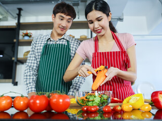 Romantic young Asian lovers happy talking, enjoy cooking healthy food together by spreading butter on toasted bread, chopping organic onion on cutting board on kitchen table of frying pan