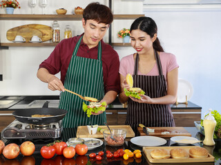 Asian chef cooking tasty food by spreading butter on toasted bread and slicing tomato into pieces on cutting board beside frying pan on gas stove, fresh vegetable for dining party.