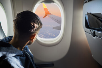 Caucasian boy is looknig into the plane porthole during the flight. Travelling concept
