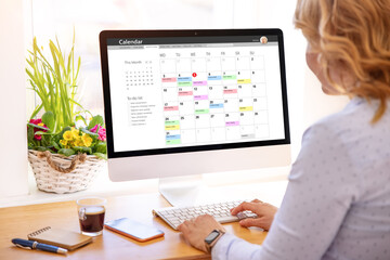 Woman using calendar app on desktop computer - obrazy, fototapety, plakaty