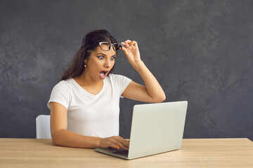 Millennial girl sit on table look at laptop screen feel shocked stunned by unexpected news online....