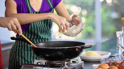 Woman professional chef pouring fresh slice of clean organic onion by hand from glass bowl into frying pan on gas stove to stir hot by spatula