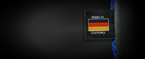 Label with German Flag and text Made in Germany sewn on a black fabric, on a black background with...