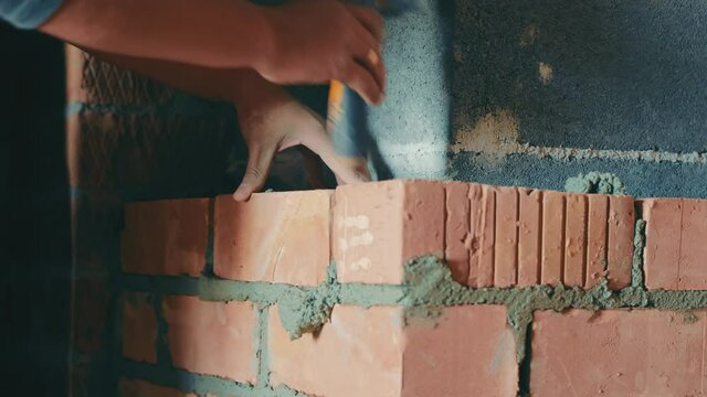 Builder lays bricks close up. A construction contractor is building a red brick ventilation duct. The builder puts bricks on the concrete mortar.