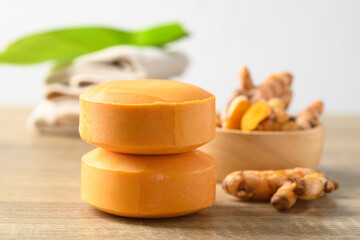 Turmeric soap and fresh turmeric root in a bowl on wooden table with white background, herbal organic soap for skin care