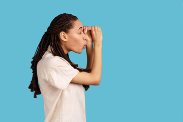 Side view of astonished woman with dreadlocks making glasses shape, looking through binoculars...