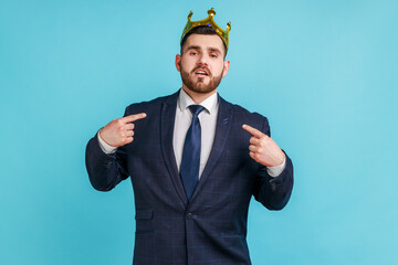 Proud bearded man wearing official style suit egoistically looking at camera, posing with crown on...
