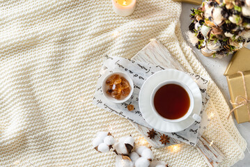 Cozy winter composition with hot tea in a cup. Cup of black tea on wooden tray on knitted plaid...