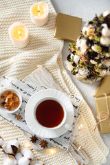Cozy winter composition flat lay. Cup of black tea on wooden tray on knitted plaid with candles, presents and Christmas tree. Christmas menu, winter tea party, social media, top view
