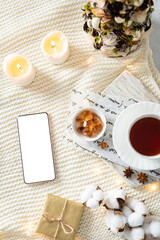 Fototapeta na wymiar Cozy Christmas composition with mobile phone, gift boxes, Christmas tree, candles and a cup of tea. Flat lay, top view, sample, copy space. Winter on line shopping, christmas sale background. Mock up