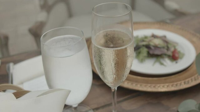 Closeup shot of a spot at a luxurious, fancy wooden dinner table with glasses of water and champagne and a plate of salad, table setting for a wedding or birthday party
