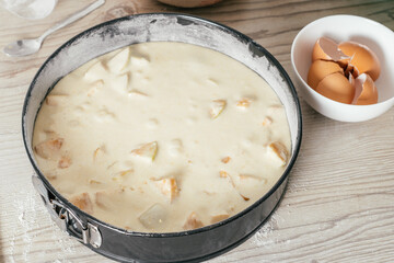 Baking dish with raw apple pie dough stands on kitchen counter next to bowl with eggshells