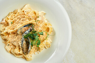 Pasta in cheese sauce with mussels and nuts on a white plate on a white tablecloth