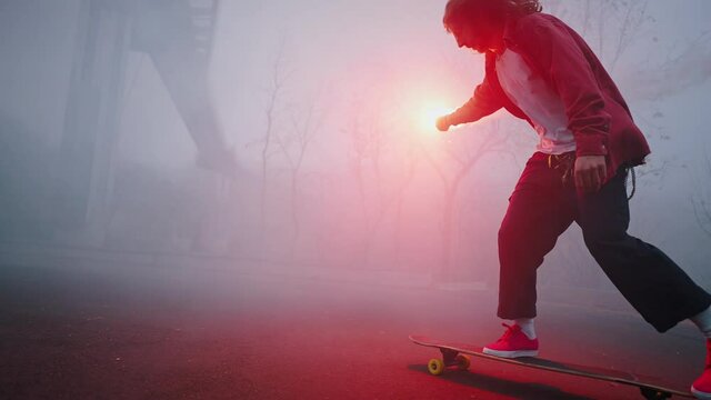 Trendy teen guy is riding a skateboard in the evening holding a red burning torch in one hand. Dangerous stunts, professional skating