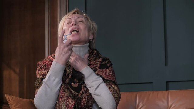 Elderly woman coughs and applies spray for sore throat at home