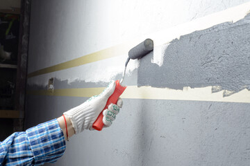 female painting a wall with masking tape and roller
