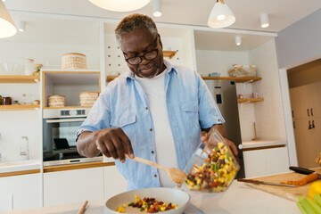 Senior African man standing in the kitchen and preparing a healthy dinner. - 472183431