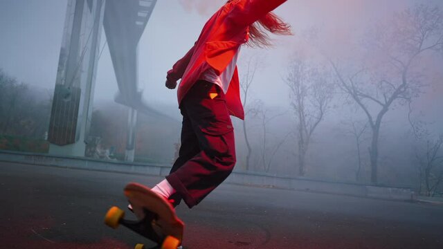 Skater performs a tail turn trick while holding a torch in one hand. Young man riding a skateboard at night with a red burning signal flare in his hand, dangerous stunts