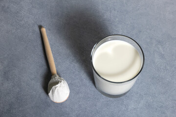 Milk in glass and full fat powdered milk in wooden spoon on grey background