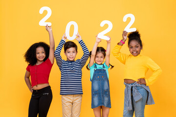 Happy cute little kids smiling and holding 2022 numbers isolated on yellow studio background for...