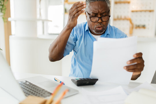 A Nervous African Pensioner Holding His Head And In The Other Hand, He Is Having Bills. He Spent Too Much This Month.