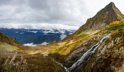 Mountain valley autumn cloudy landscape with waterfall and snow