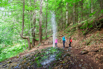 Geyser fountain of cold water in the summer forest. Family at tourist nature attraction