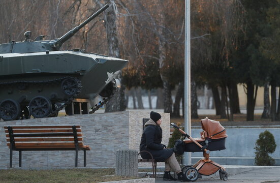 A woman sits with a baby stroller next to an infantry fighting vehicle installed as a monument in a park in Kramatorsk