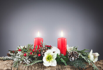 Christmas decoration  made with cork bark, pine, white flowers, red berries, red candles with hot flame, pine cones and snowy branches on gray background