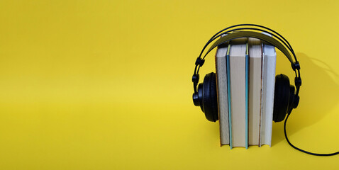 Books set upright with black headphones on top on a yellow background. Text space. Audio book...