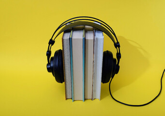 Books set upright with black headphones on top on a yellow background. Text space. Audio book concept. Minimal style.