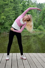 Fototapeta na wymiar Young and slim woman exercising in park with pond. Polish woman doing some yoga and stretching.