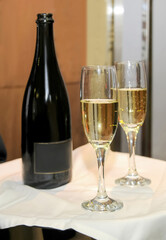 Close up view of a crystal glass with champagne near another full glass and a bottle of champagne on a tray.