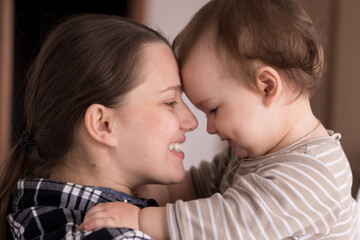 Portrait Adorable Face Of Little Cheerful Happy Toddler baby girl child With Charming Smile Look At Mom Strong Cuddles Loving Mommy Together. Mother Hugs play love care kiss smiling daughter at home