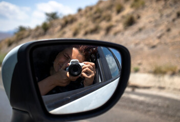 The woman taking photos with her camera in the car takes pictures of herself in the rearview mirror. - Powered by Adobe