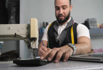 Tailor shop owner calculating monthly reports, bills and expenses of his small business.  Small...