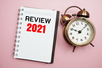 Review 2021 text with alarm clock on pink background