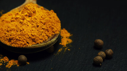 Turmeric in a wooden spoon and allspice on a black table.