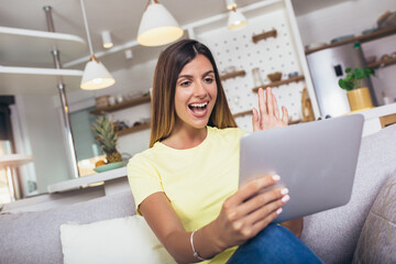 Young woman resting on couch hold digital tablet look at device screen smiles enjoy online chat with boyfriend