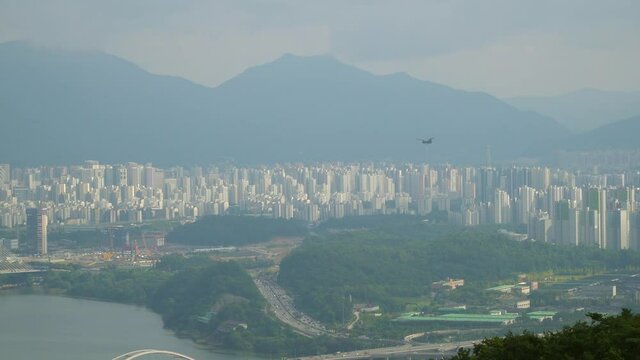 Boeing CH-47 Chinook cargo helicopter flying over Seoul on urban city skyline and mountains background on hazy day, view from Acha mountain peak aerial