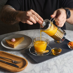 sea buckthorn tea with cloves and other spices in a glass teapot and a cup in which tea is poured on a dark background