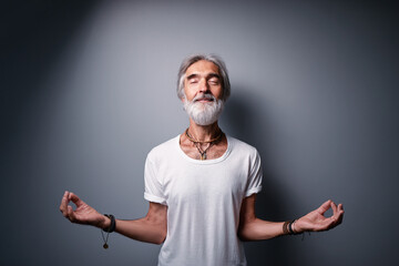 Studio portrait of senior bearded man in lotus pose. Concept of calm and meditation.