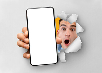 Shocked man showing white empty smartphone screen breaking through paper