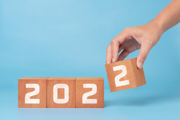 Happy new year 2022. new year background concept with blue background, Hand putting wooden cube to complate 2022 text.