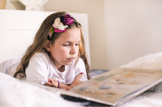 Schoolgirl reading a book in the room. Girl 8 or 10 years old with a book in the room on the bed. A child in a bright interior to study at home. Copy space. High quality photo